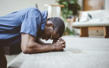 African-American male praying on his knees with his head down at the church